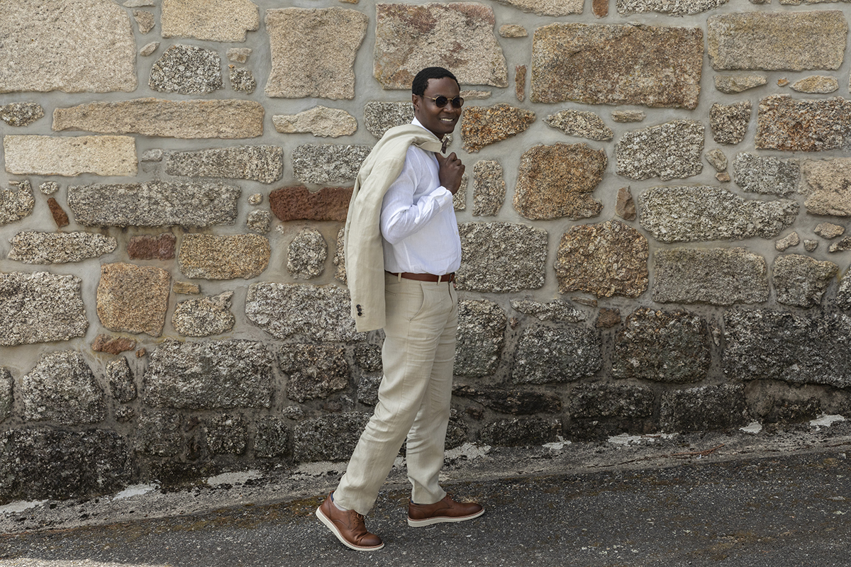 Numa rua inclinada, Hélder caminha com o casaco ao ombro. O sorriso descontraído revela o conforto de quem está prestes a dizer “sim”.