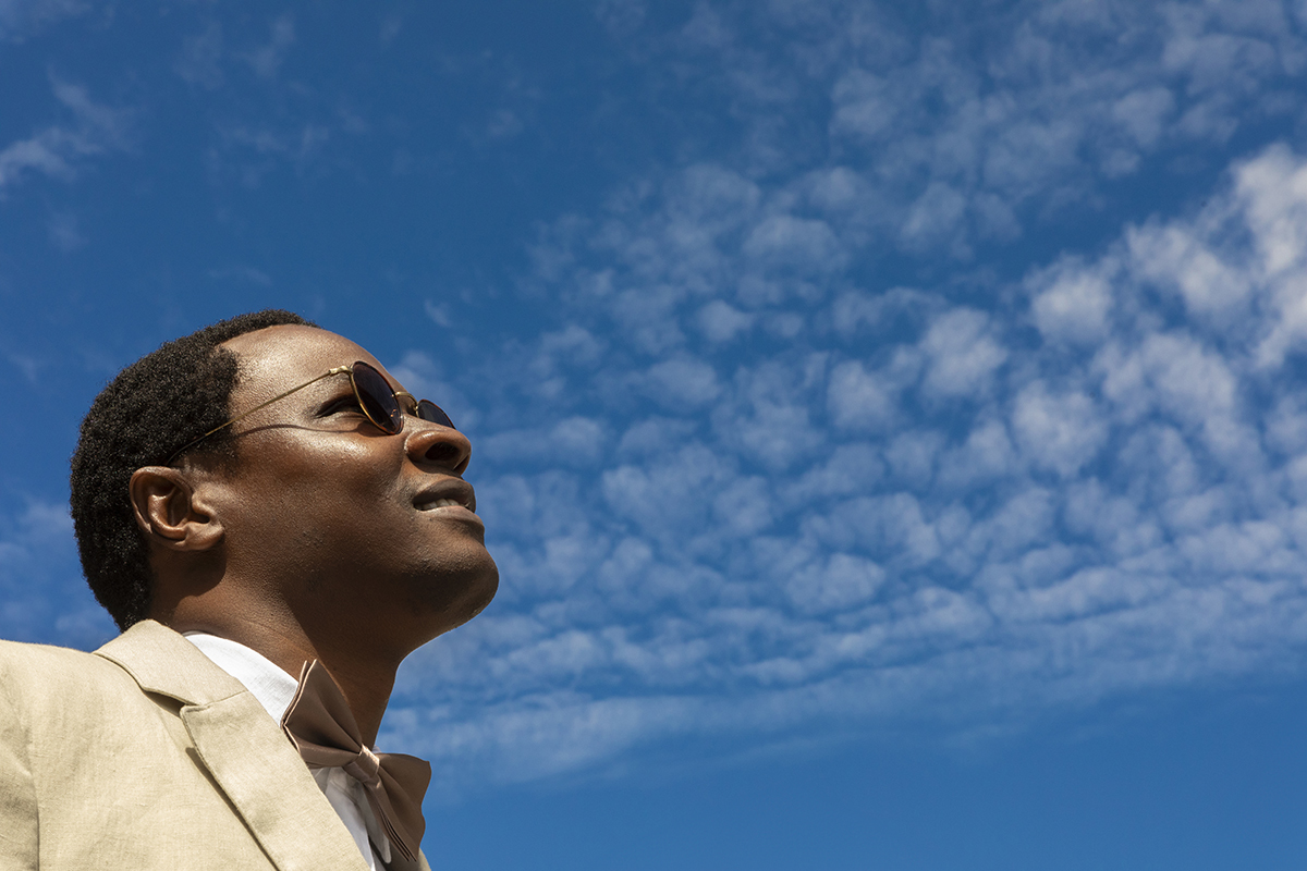 De rosto erguido, Hélder observa o céu limpo. O ângulo contrapicado reforça a simbologia: um noivo confiante, pronto para o que vem.