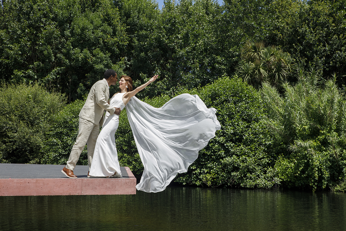 Num momento de pura leveza e cumplicidade, o casal arrisca um passo em direção ao inesperado. O vestido da noiva dança com o vento, como se voasse, enquanto ele a segura com firmeza e ternura. Uma imagem que parece saída de um sonho.