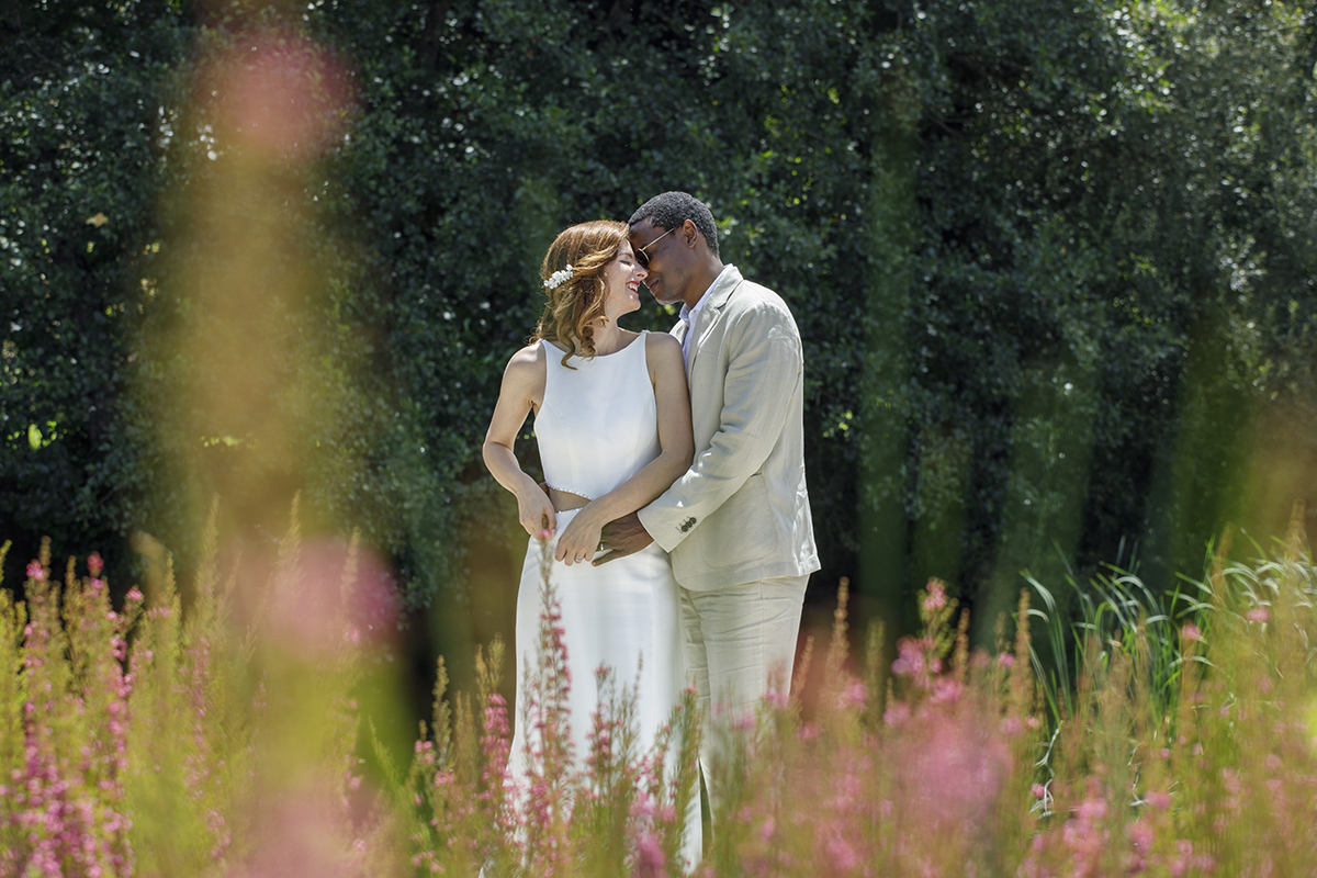 Entre flores rosa desfocadas, os rostos aproximam-se num beijo doce. Um gesto simples que espelha a pureza do amor partilhado.