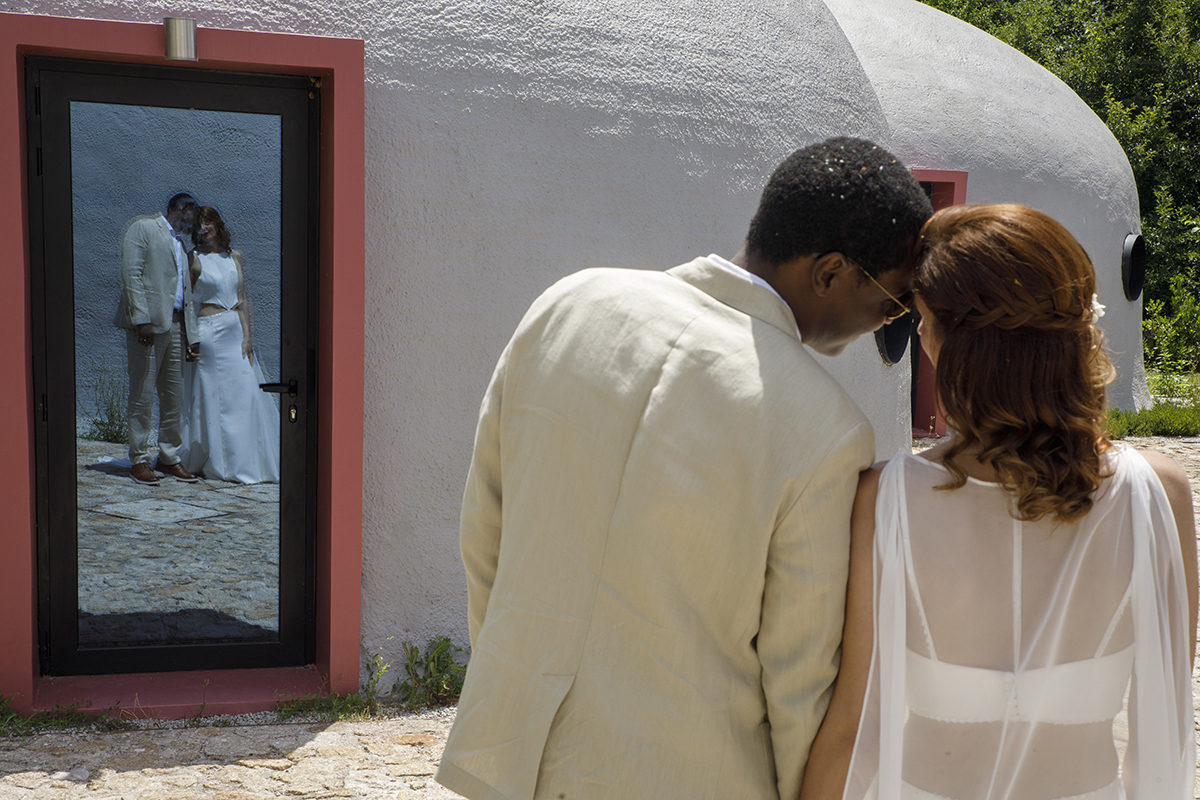 Cabeças encostadas, olhares trocados, e um reflexo na porta da casa. Uma imagem que transmite ternura e cumplicidade.