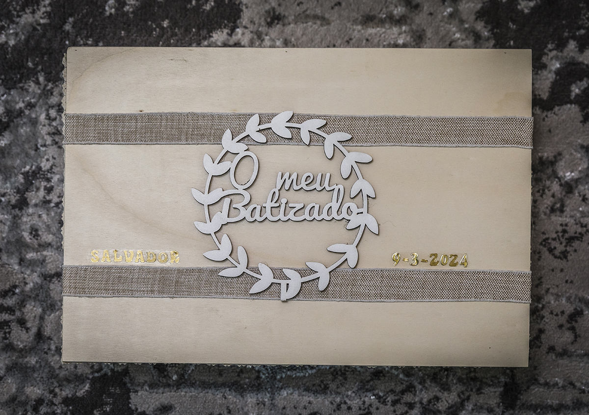 Placa de madeira delicadamente decorada com folhas brancas em roda. No centro, lê-se 