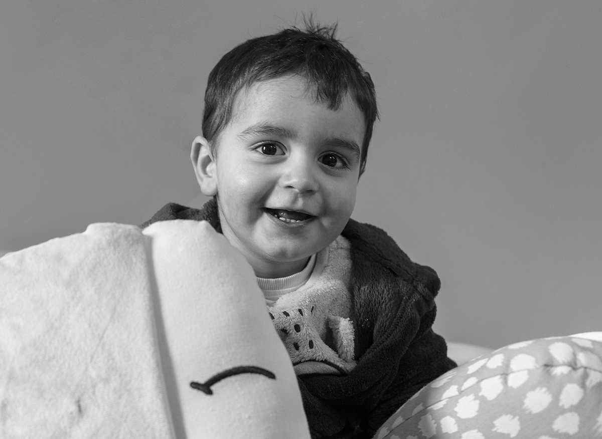Em preto e branco, Salvador solta um sorriso contagiante. À sua volta, os peluches parecem sorrir com ele, numa imagem cheia de vida e inocência.