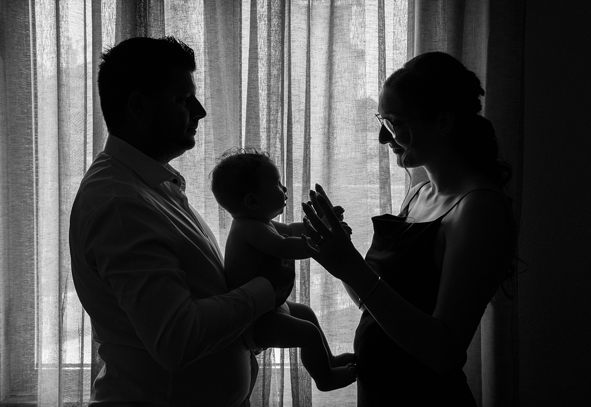 Uma foto em preto e branco onde o pai o segura ao colo, virados para a mãe que lhe dá as mãos. O cenário ao pé da janela, com a luz a entrar, cria um efeito de silhueta incrível, um efeito muito bem pensado por Ricardo Coimbra Fotografia.