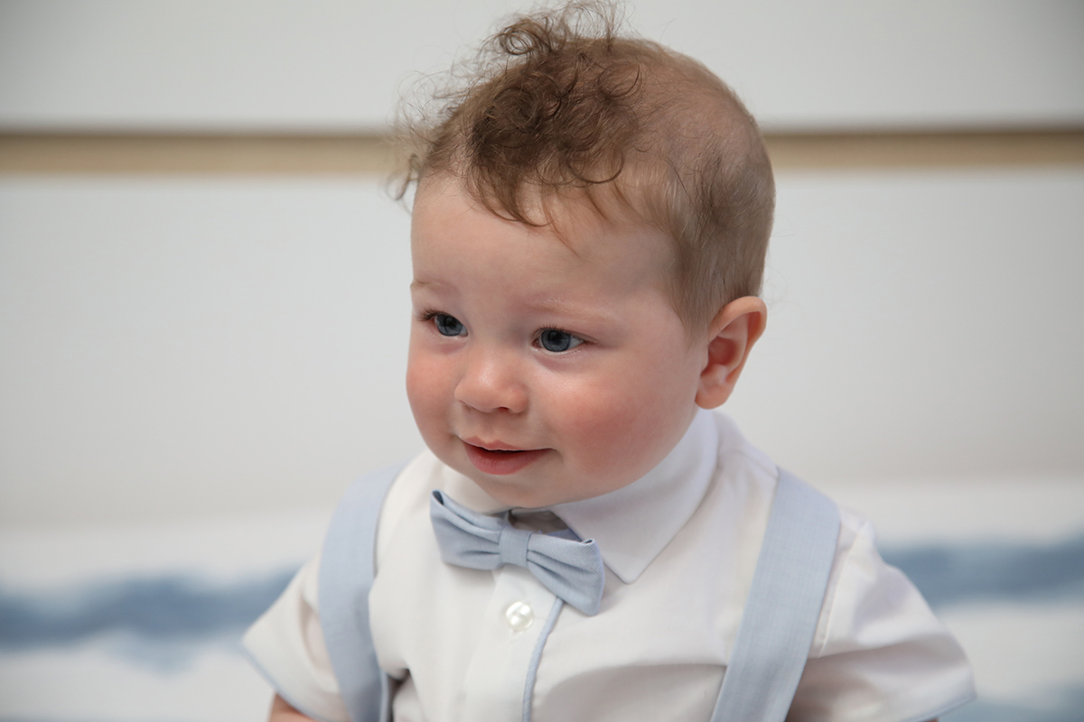 Com um olhar curioso, o pequeno Mário fixa algo à sua frente, começando a abrir um sorriso que promete iluminar o momento. Fotografia batismo Tondela