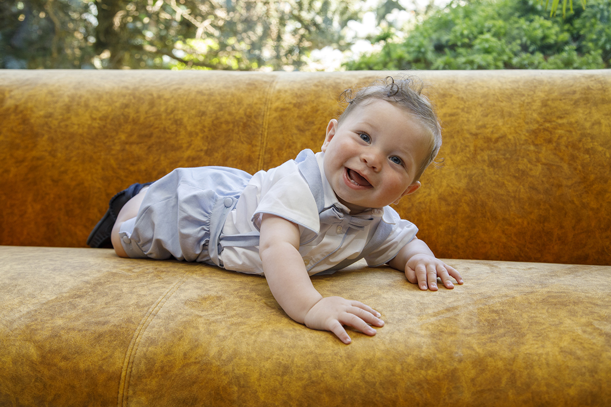 Entre almofadas, o pequeno Mário solta expressões de pura alegria, como se gargalhasse com o coração, contagiando quem o vê.