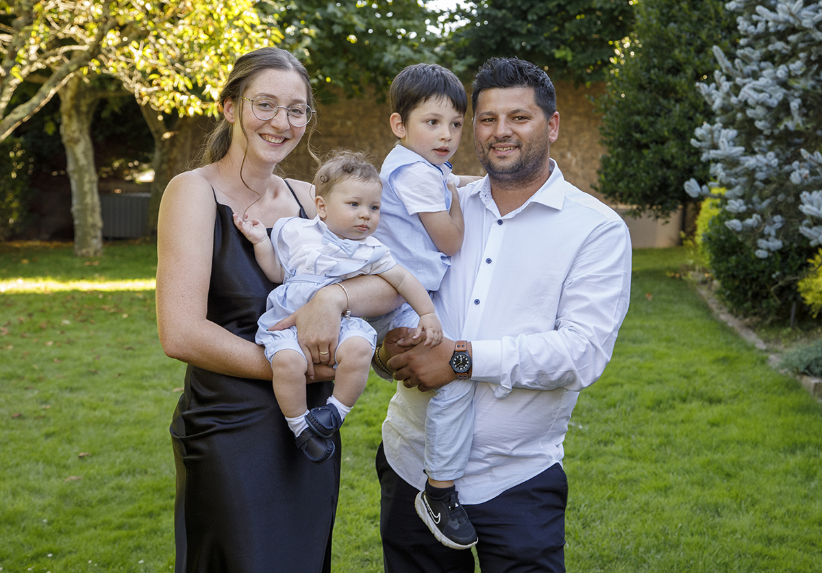 Num jardim iluminado pelo sol, a família reúne-se em harmonia. Os pais sorriem com ternura, enquanto os filhos, mais sérios, estão ao colo, o Mário com a mãe, o irmão com o pai. Restaurante Dao Catering