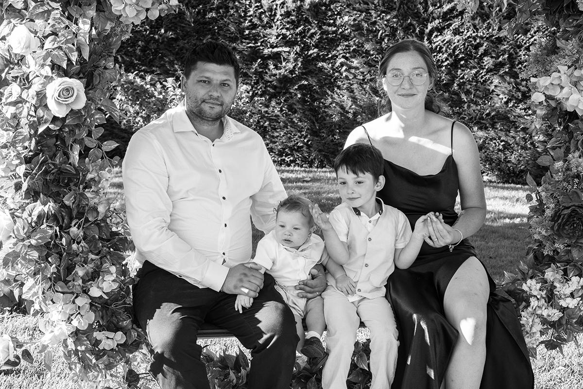 Em preto e branco, a família está sentada numa roda florida. De mãos dadas e corações unidos, sorriem com uma felicidade que se sente, mesmo sem cor.