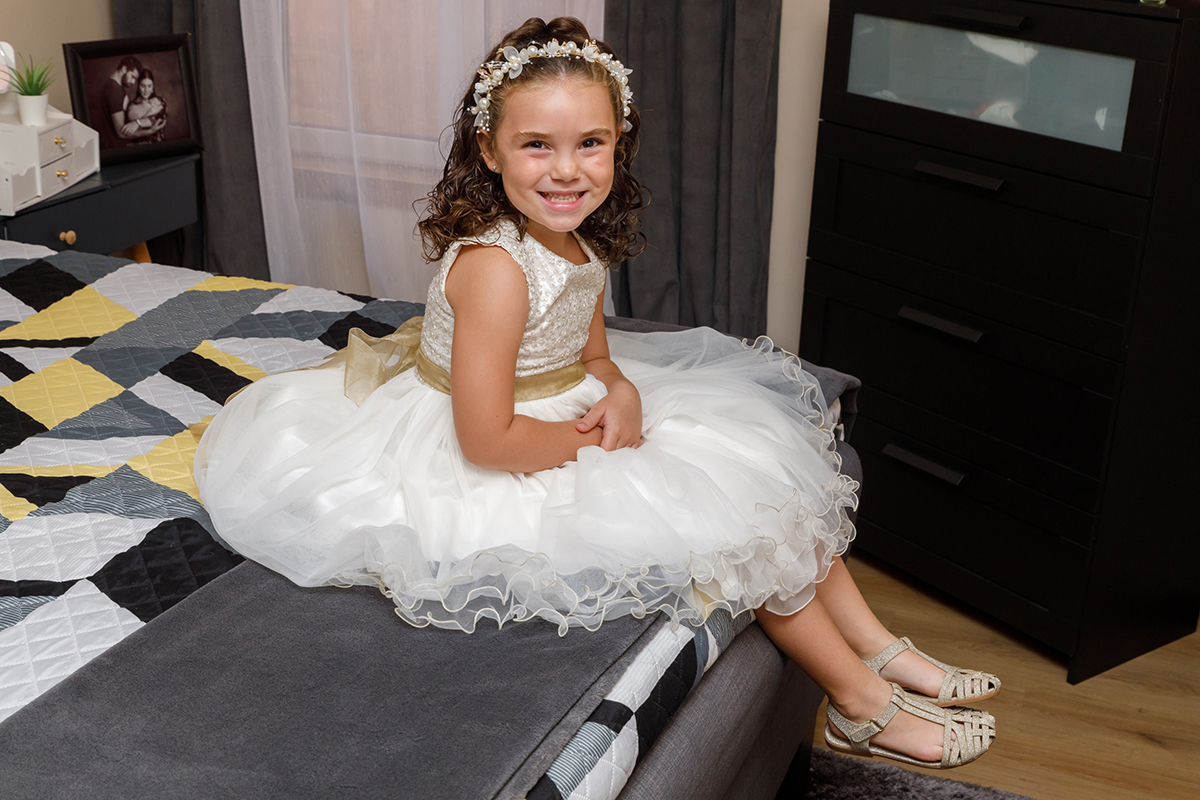 Iris, já vestida, sorri para a câmara, irradiando felicidade num dos momentos mais doces da sessão de batizado.