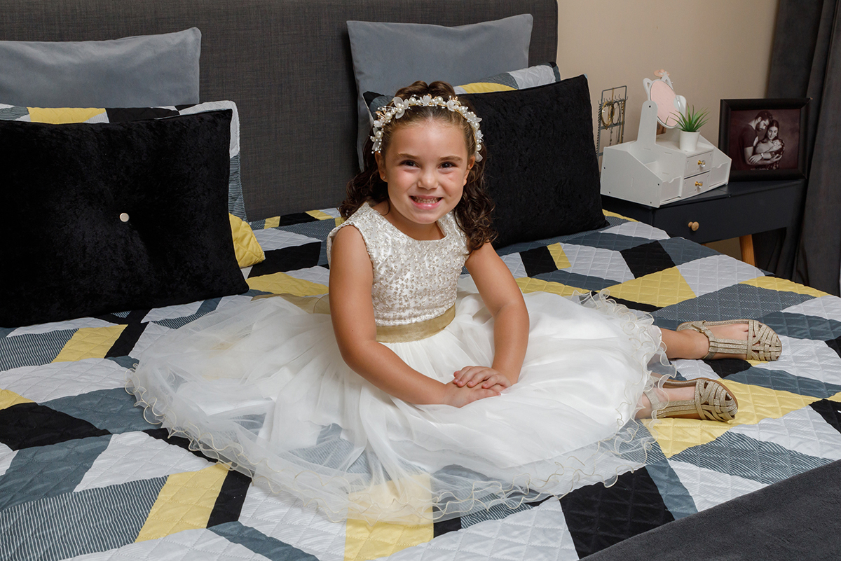 Sentada na cama, com as mãos pousadas nas pernas e um sorriso sereno, Iris deixa transparecer a sua felicidade.