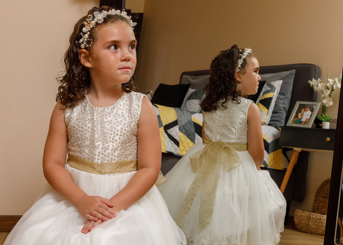 Virada para o lado, Iris surge pensativa mas feliz, o espelho atrás revela o delicado laço nas costas do vestido.