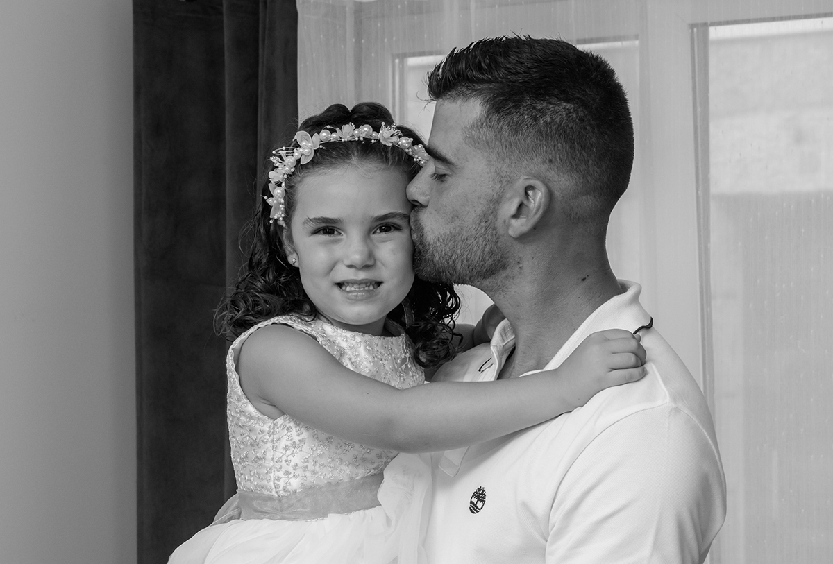 Num gesto cheio de ternura, o pai dá um beijinho na bochecha da Iris, que sorri abertamente, feliz da vida.