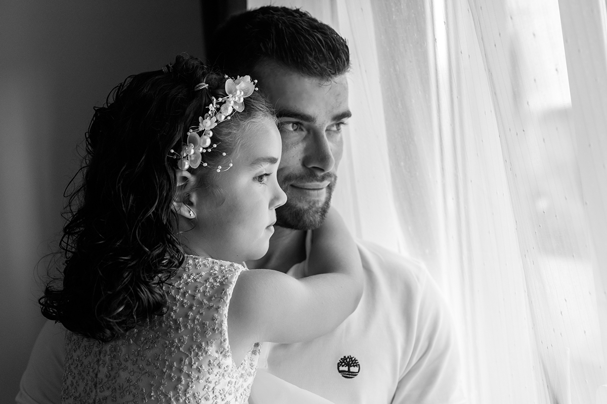 Ao colo do pai, Iris abraça-o com carinho, ambos olham pela janela, com um sorriso discreto e um ar sonhador.