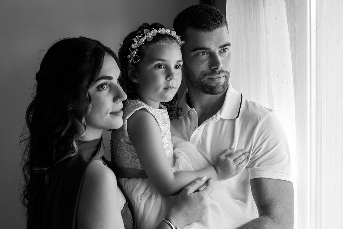 Os pais de Iris seguram-na ao colo, num instante de união e calma, marcado por sorrisos leves e olhares cúmplices.