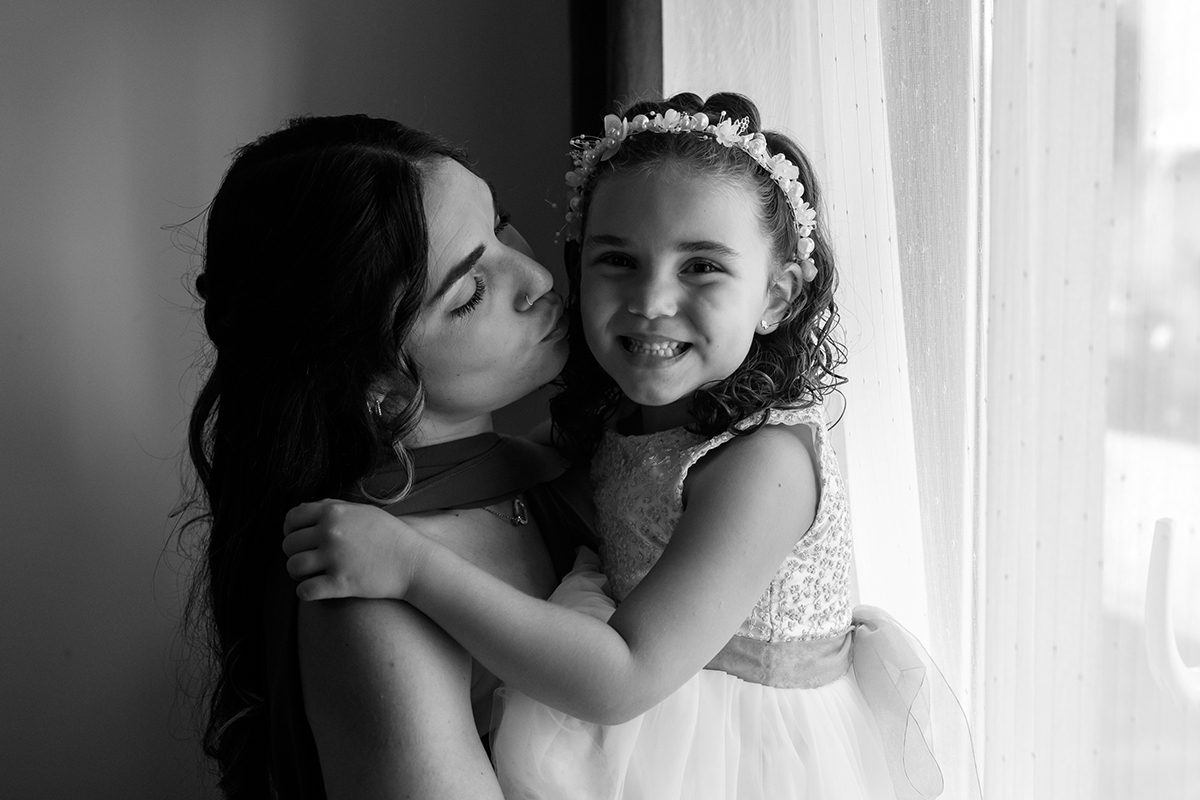 No colo da mãe, Iris recebe um beijinho doce e retribui com um sorriso enorme, cheio de alegria.