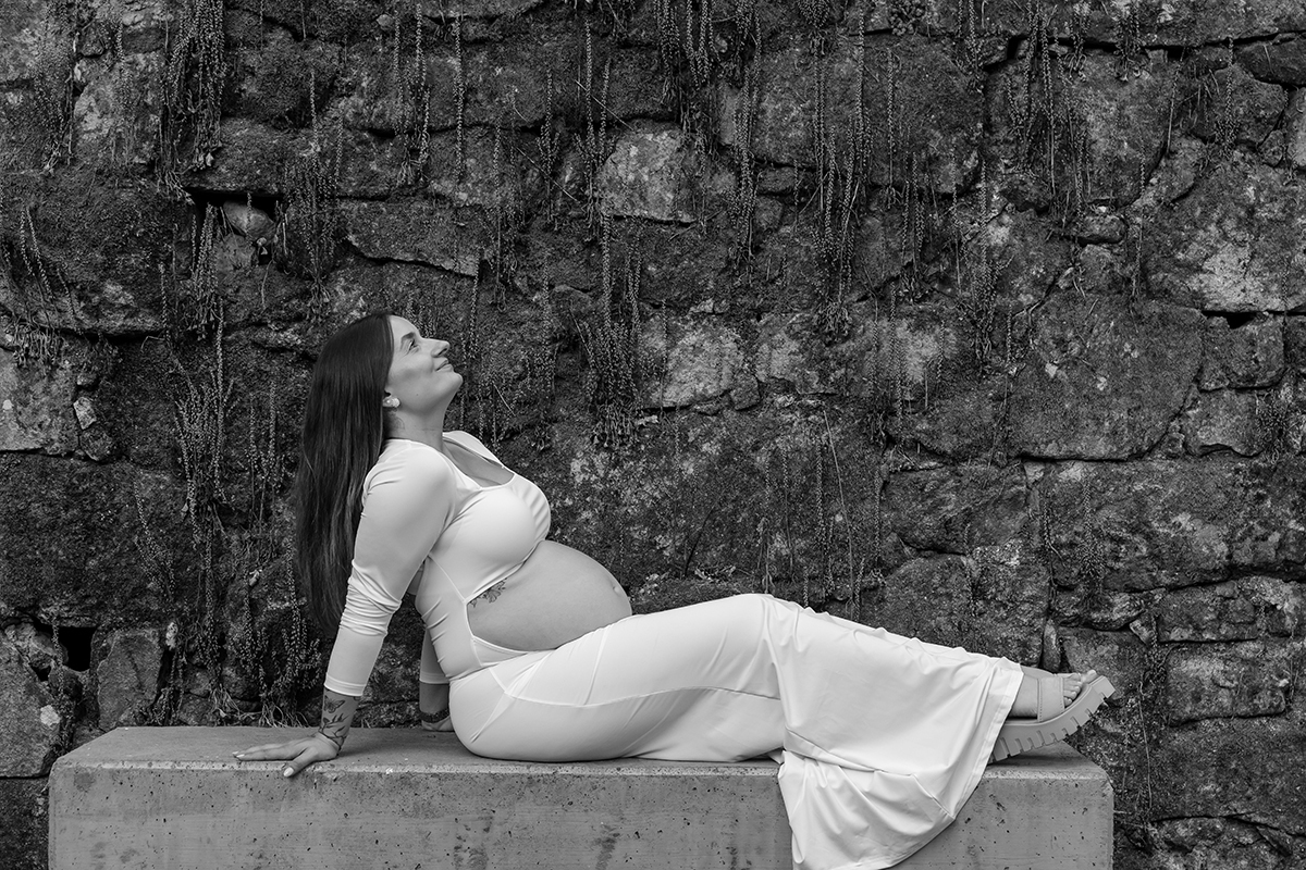 Linda foto desta Grávida deitada em banco de pedra com fundo rústico