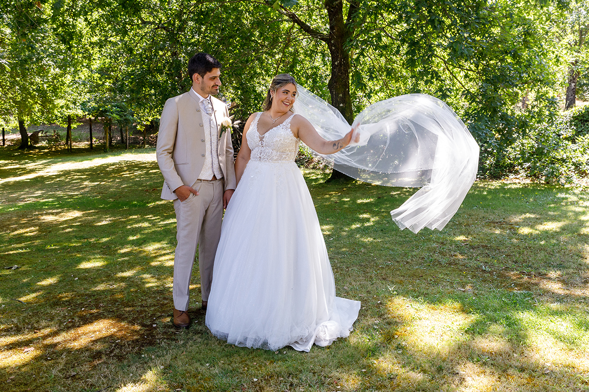 Noiva em pé ao ar livre, com vestido branco esvoaçante e véu longo, rodeada de natureza, num momento tranquilo captado por fotógrafos-casamento-tondela-viseu em sessão de fotografia-casamento com luz natural.