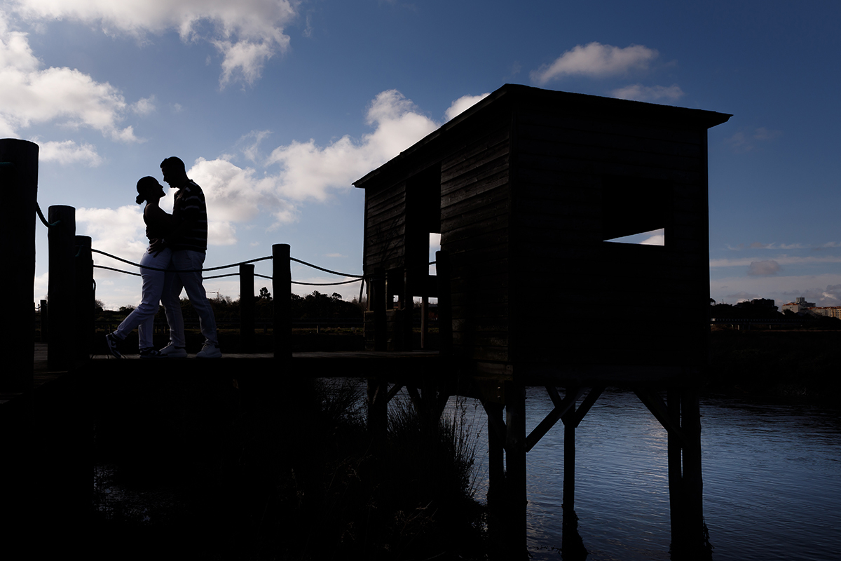 Vanessa e Philippe caminham de mãos dadas nos passadiços de Aveiro ao pôr do sol.