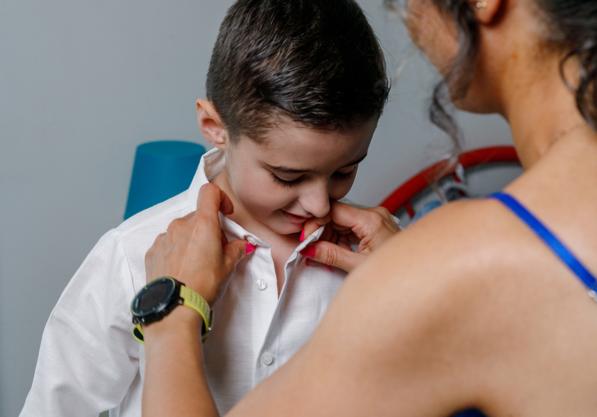 Mãos da mãe a abotoar a roupa de batismo do Salvador na sua casa em Carregal do Sal.