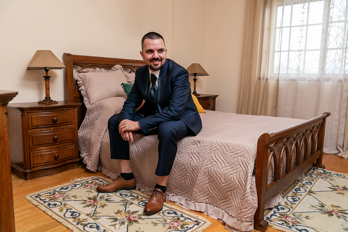 Preparação do noivo em casa, sentado na cama em ambiente intimista antes do casamento no Caramulo, fotografia documental por Fotocoimbra, fotógrafos de casamento Tondela e Viseu.