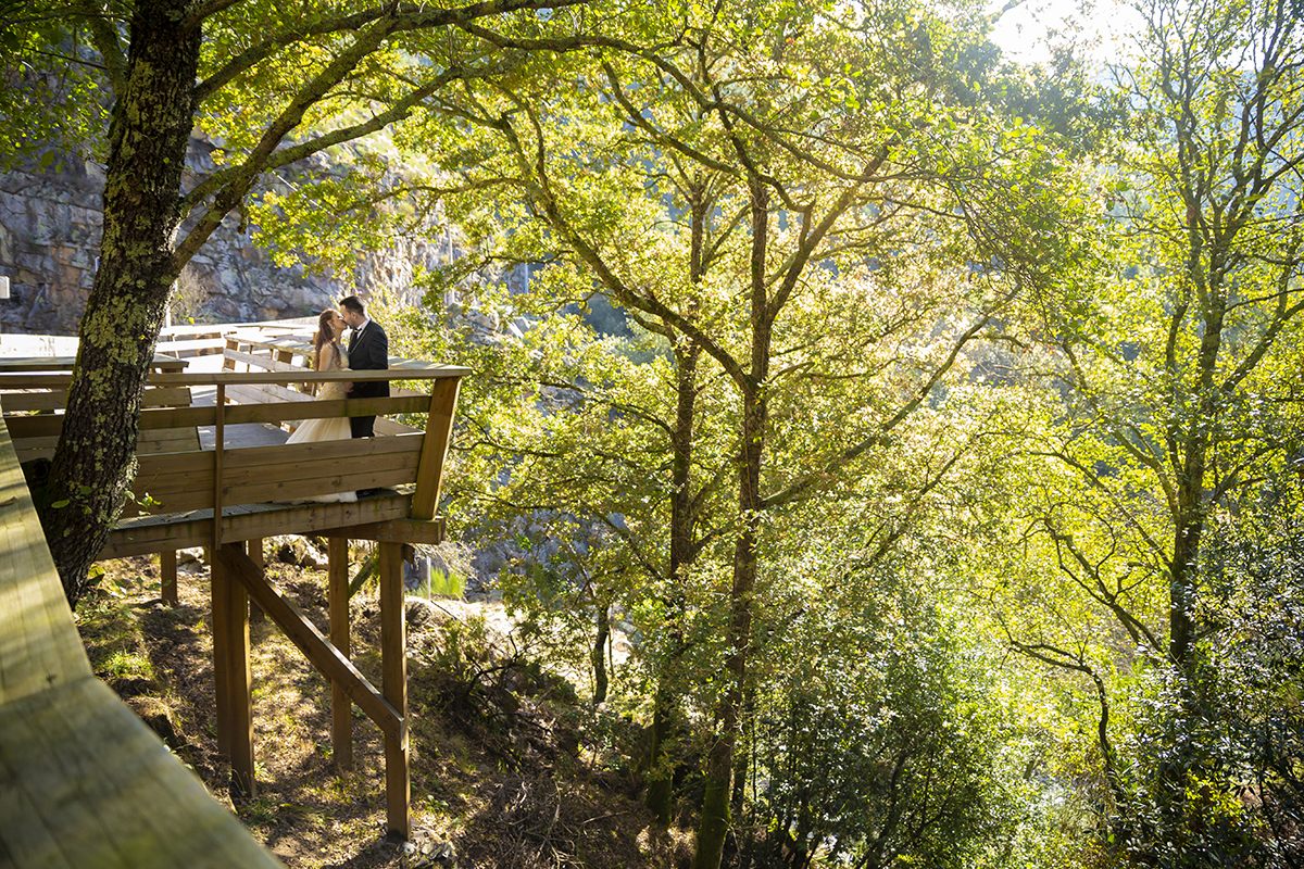 Num plano mais afastado, Jorge encosta-se ao corrimão enquanto Daniela, diante dele, se entrega a um beijo sereno. Ao fundo, a natureza observa, em silêncio, este instante de amor emoldurado pela paisagem viva.