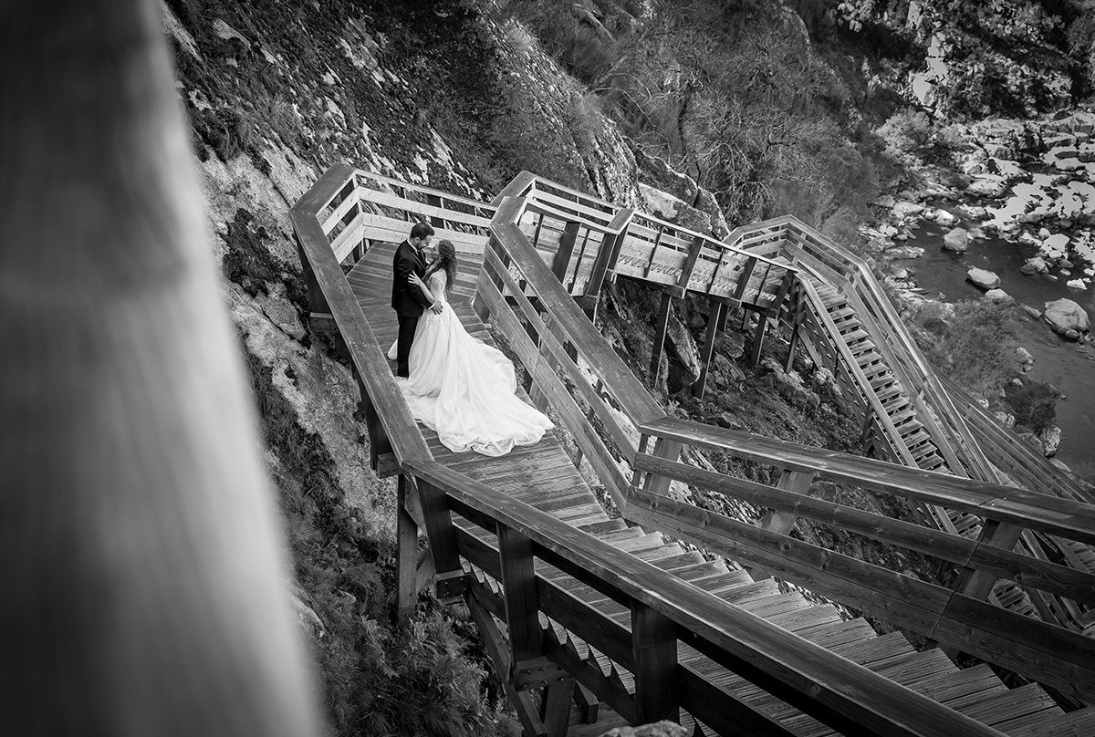 A preto e branco, a fotografia ganha um toque intemporal. Vistos de cima, os dois estão frente a frente nos passadiços. Jorge envolve Daniela pela cintura, enquanto ela pousa as mãos sobre as dele, num gesto cheio de ternura.