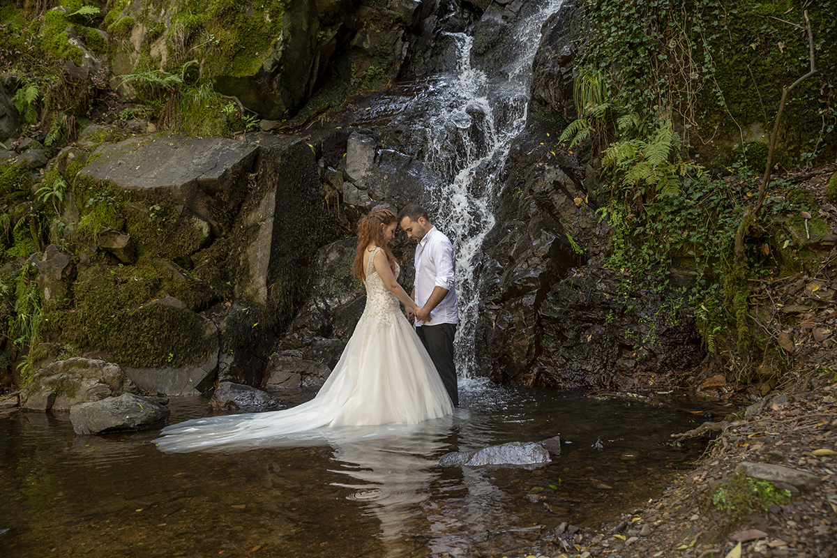 Dentro de um ribeiro, com a água a correr e uma cascata atrás, os dois surgem de mãos dadas, as cabeças encostadas. Um momento poético, onde a natureza se funde com o romance.