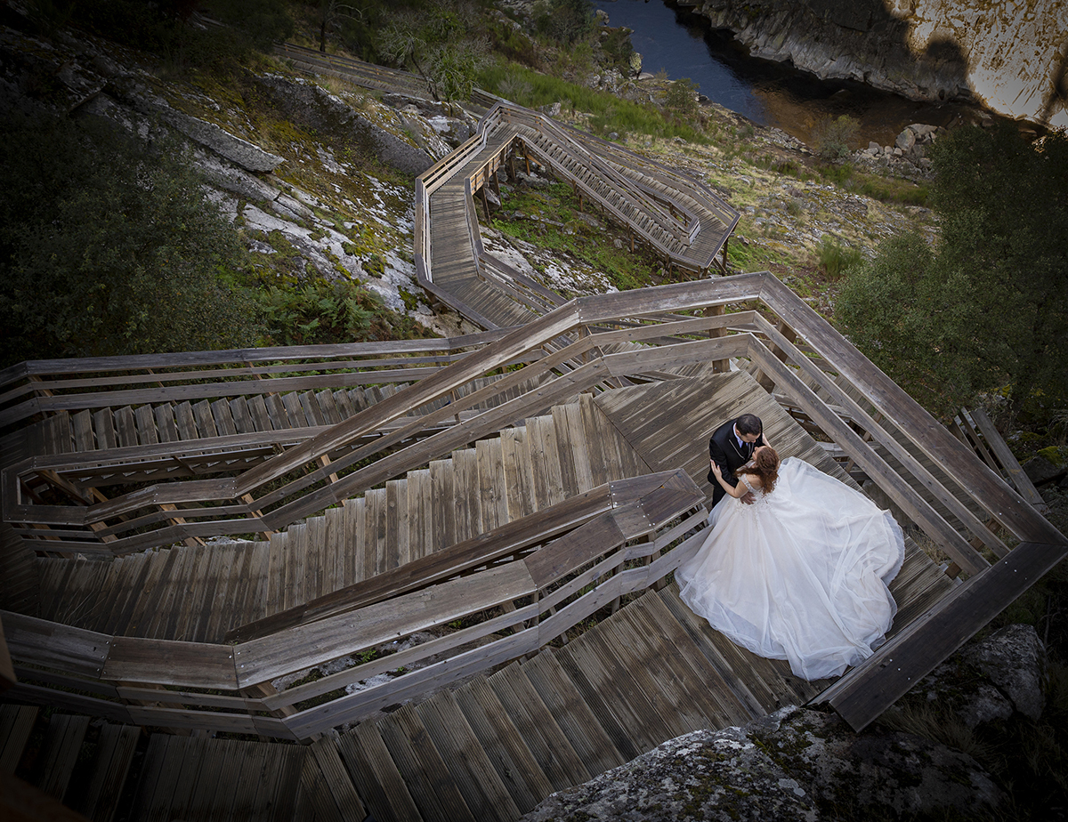 Com vinheta suave e tirada de cima, esta imagem mostra os dois no meio das escadas dos passadiços, frente a frente, abraçados pela cintura. Um momento íntimo visto de uma perspetiva elevada.