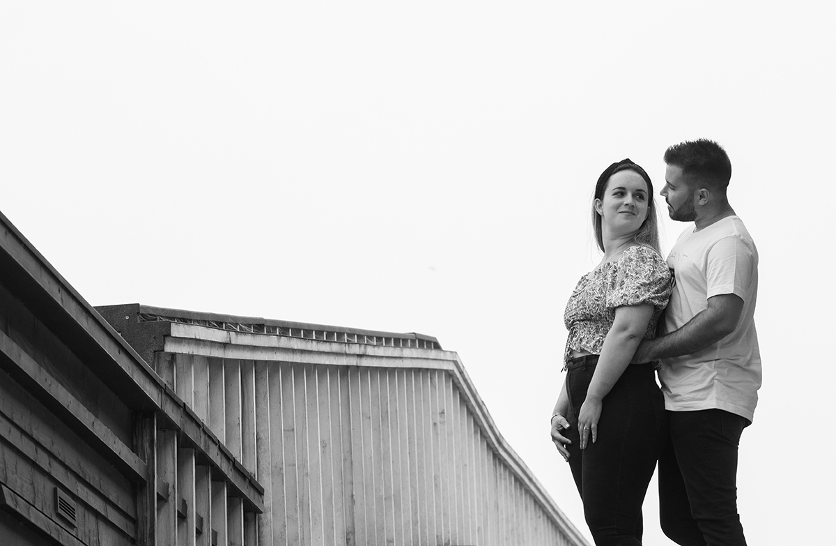 Em preto e branco e com ternura suspensa no tempo, os dois surgem no lado direito da imagem, Ricardo envolve Marta pela cintura com um carinho que parece dançar no silêncio, enquanto ela, de costas mas com o rosto virado para ele, retribui-lhe o olhar.