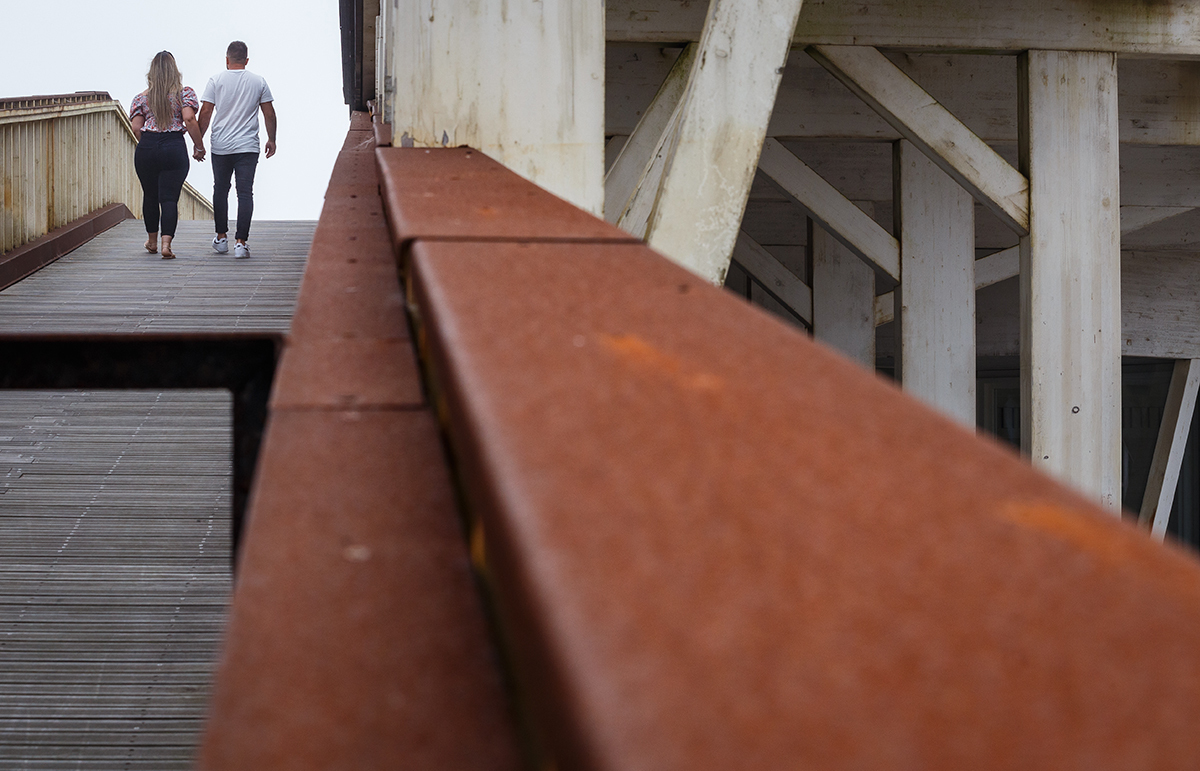 A câmara repousa sobre um corrimão alaranjado que talvez tenha nascido da ferrugem ou da arte do tempo, e por entre os passadiços de madeira ao fundo, Marta e Ricardo caminham de mãos dadas, com os corações alinhados, lado a lado.