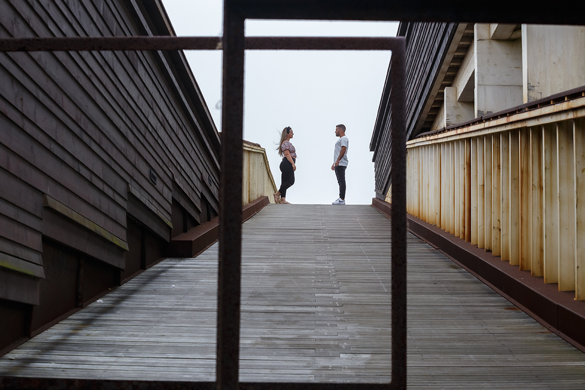 Entre estruturas metálicas que se entrelaçam sobre os passadiços, forma-se um retângulo vertical, uma moldura natural que emoldura ao fundo os dois pombinhos frente a frente, sérios mas doces, num momento íntimo que talvez guarde pensamentos partilhados.