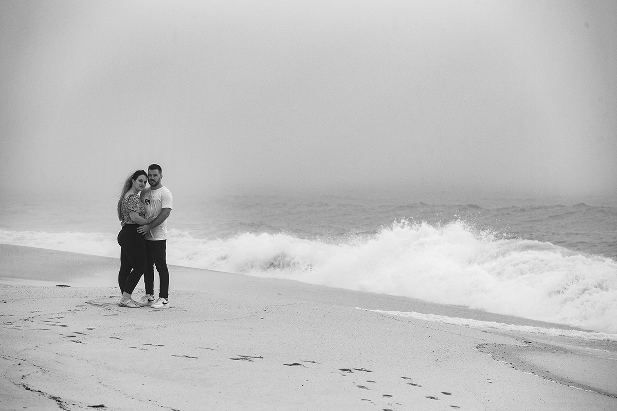 Aqui vemos os dois no lado esquerdo da imagem, ao pé do mar, virados um para o outro, abraçados pela cintura e a olharem para a câmara de Ricardo Coimbra Fotografia com uma alegria serena que aquece a alma.