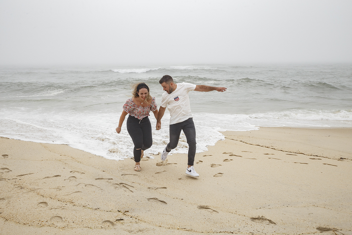Aqui vemos os dois ao pé do mar, a correrem de mãos dadas a tentarem fugir da água, com o mar mesmo juntinho aos pés num momento divertido e cheio de riso leve.