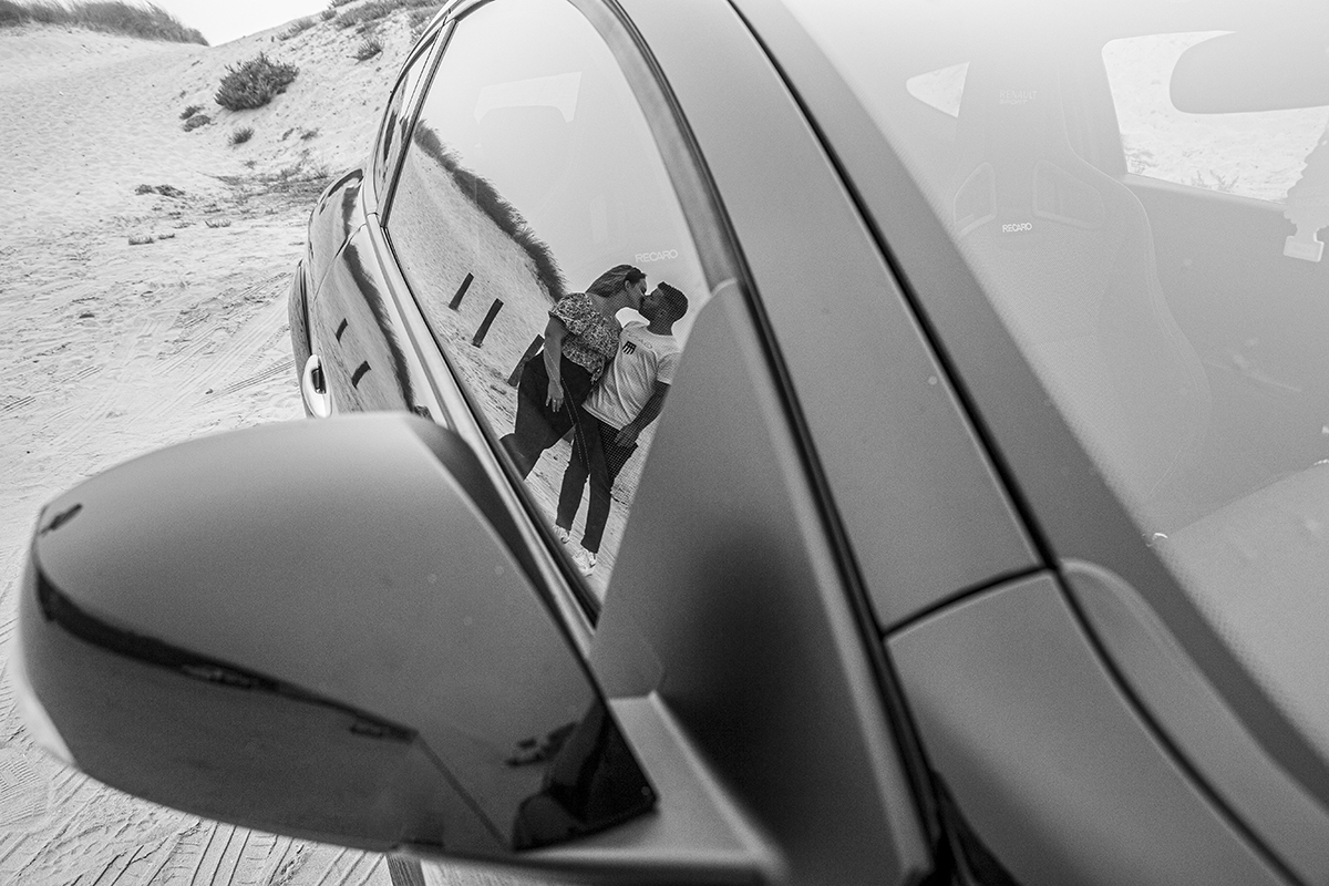 Aqui vemos um plano mais aproximado junto à janela do carro, onde vemos o reflexo dos dois na mesma posição, mas desta vez estão a beijar-se, como se até o vidro guardasse o segredo do amor.