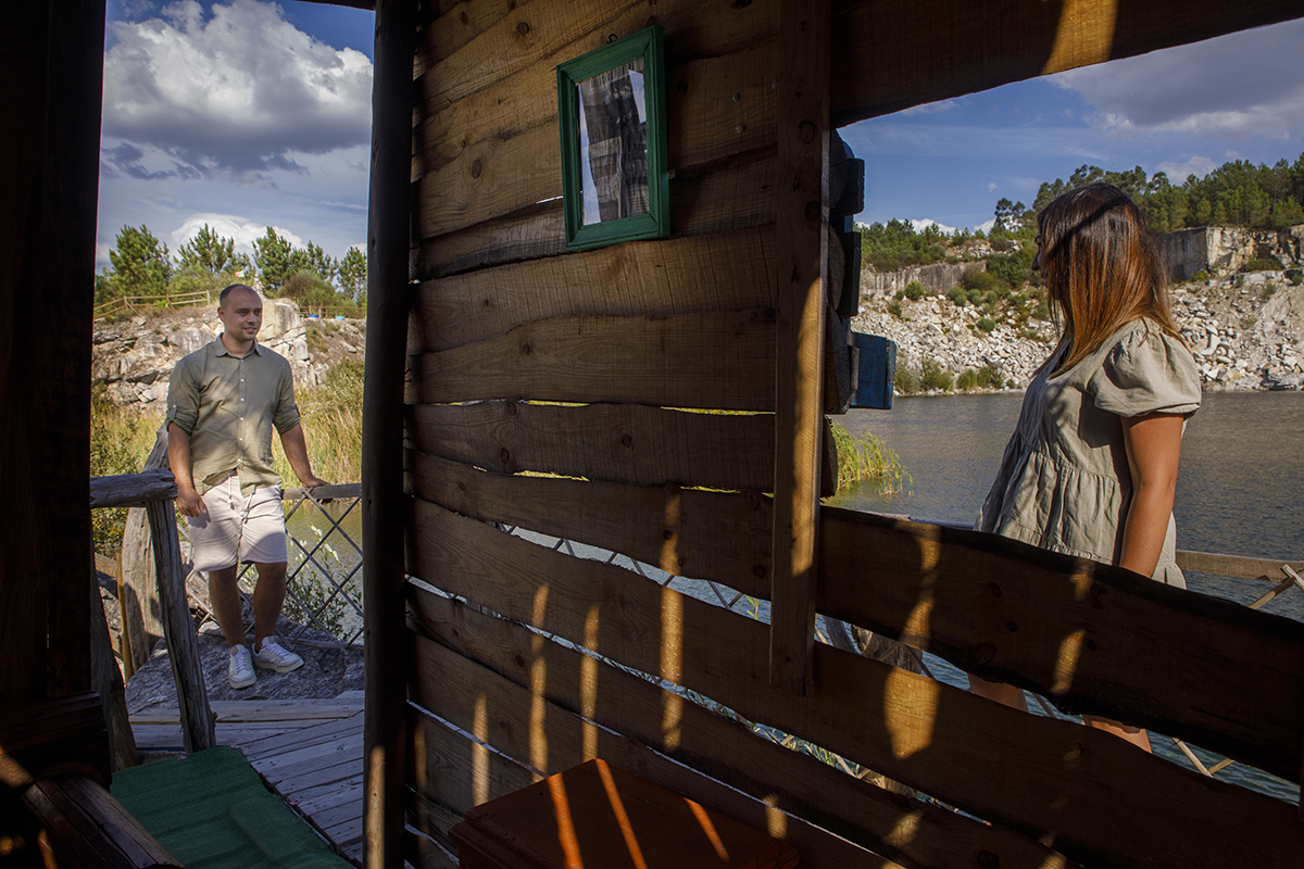 Através da moldura de madeira de uma janela simples, vemos Patrícia por dentro da casa a olhar com ternura para Bruno, que surge sorridente à porta. Há um carinho quase cinematográfico no modo como os dois se observam.