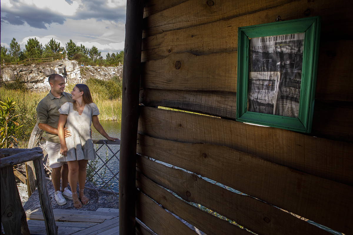 Mais próximo, dentro da mesma porta de madeira, Bruno envolve Patrícia num abraço apertado por trás, enquanto ela sorri e o olha de lado. A ternura do gesto enche o espaço, como se aquele abraço fosse morada e promessa ao mesmo tempo.