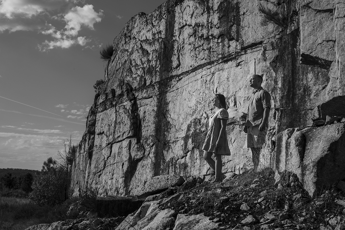 Ainda no mesmo cenário rochoso, mas agora a preto e branco, vemos os dois de corpo inteiro, lado a lado no alto da pedra. Bruno ligeiramente mais atrás, ambos com os olhos fechados e os rostos voltados para cima, num momento de paz e introspeção.