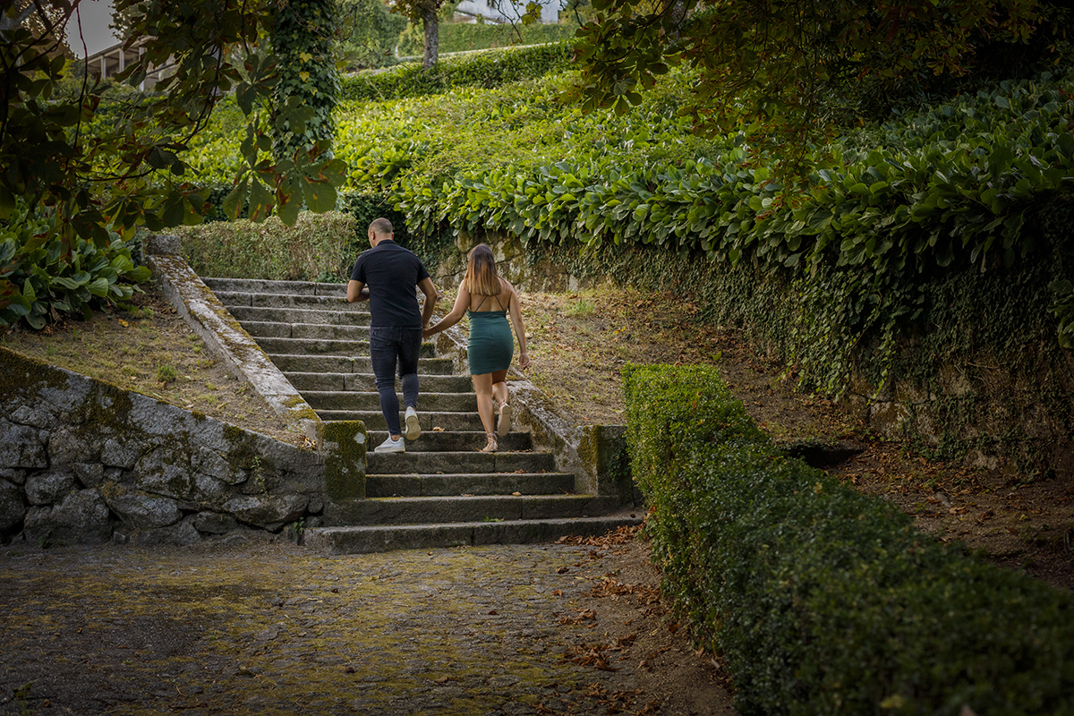 Com uma vinheta suave a emoldurar a imagem, os dois sobem umas escadas de jardim, de mãos dadas, vistos de costas. A luz branda recorta as silhuetas enquanto avançam, degrau a degrau, como se a felicidade morasse no topo.