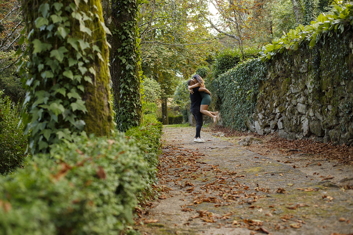 No meio de um caminho coberto por folhas castanhas, ladeado por muros e árvores com musgo, os dois abraçam-se intensamente. Bruno levanta Patrícia num gesto de carinho e alegria, e a imagem respira outono e paixão.