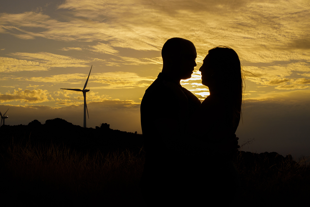 Nesta última silhueta, os dois estão de frente um para o outro, abraçados, sob o fogo dourado do pôr do sol, enquanto a ventoinha eólica se recorta contra o céu pintado de cores quentes, criando uma atmosfera de magia e eternidade.