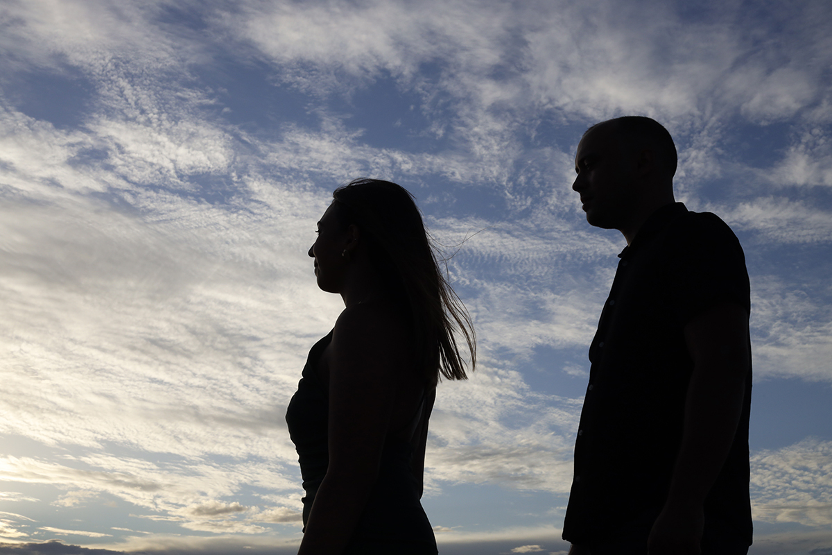 Outra silhueta, agora num plano mais aproximado da cintura para cima, revela os dois virados de perfil para a câmara, serenos e em comunhão perfeita com o momento e a paisagem.