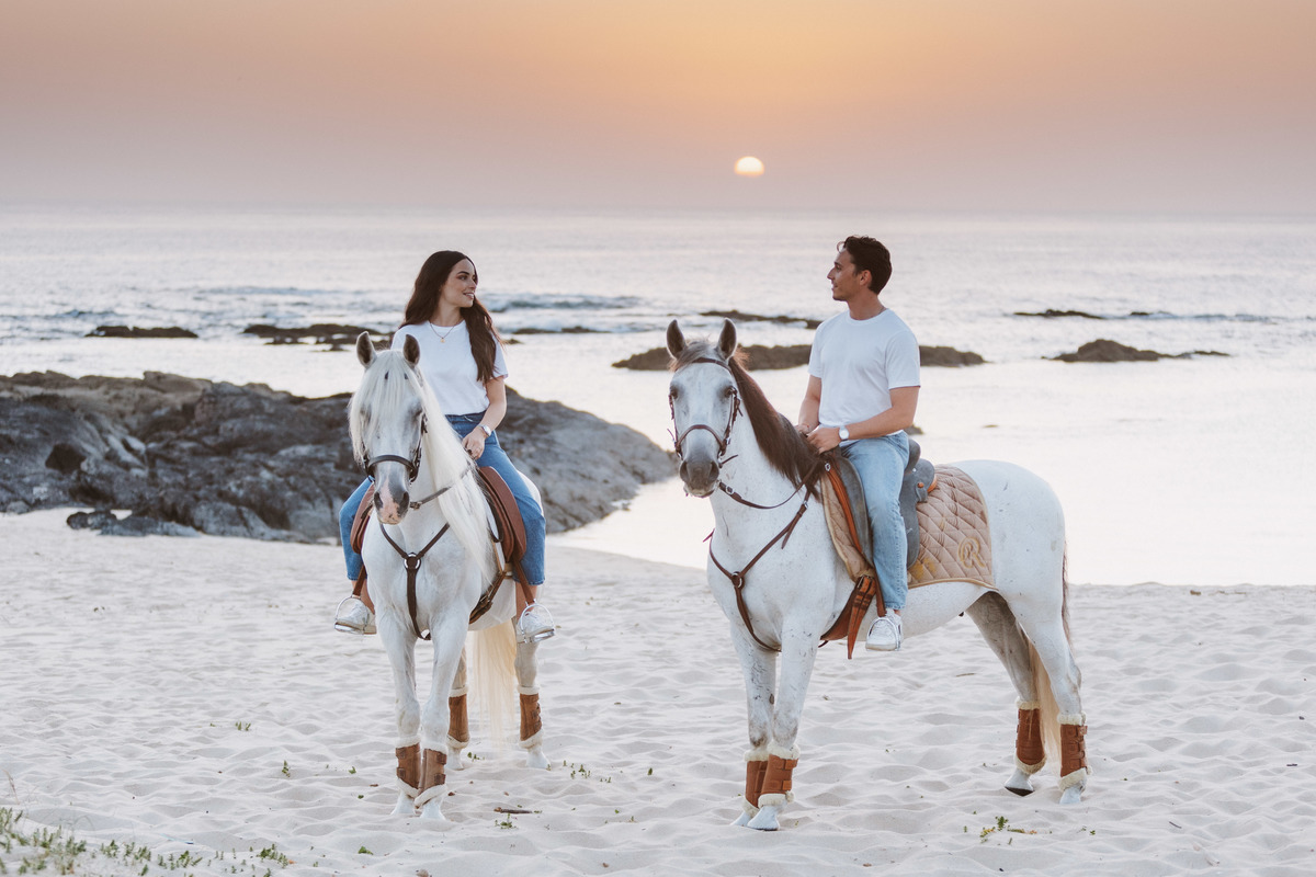 Sessão fotográfica pré-casamento junto ao mar, casal com cavalos em ambiente natural.