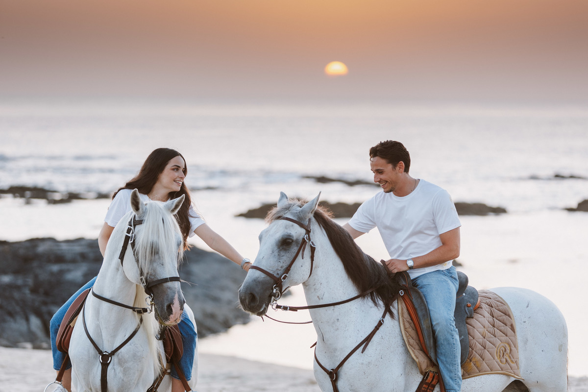 Retrato de casal em sessão de solteiros na praia, luz natural de pôr do sol.