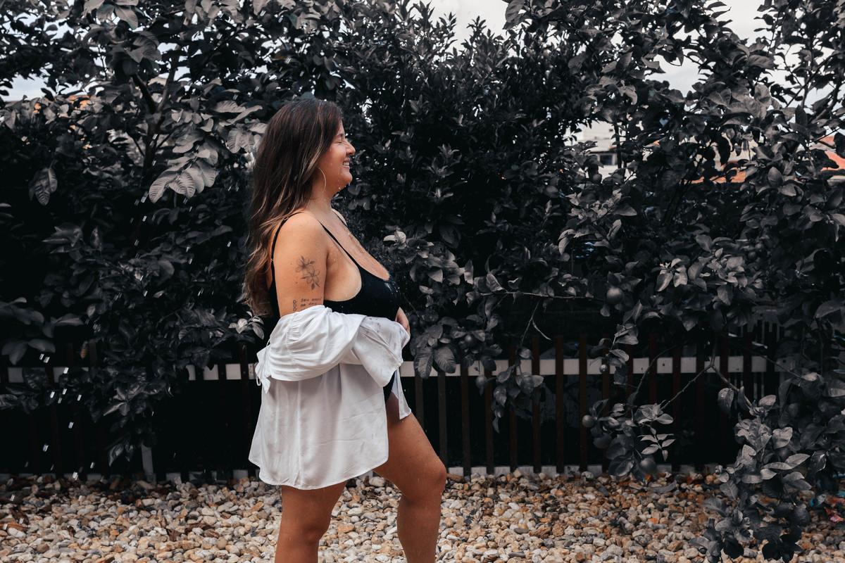 foto de mulher de body preto e camisa branca sendo molhada por mangueira