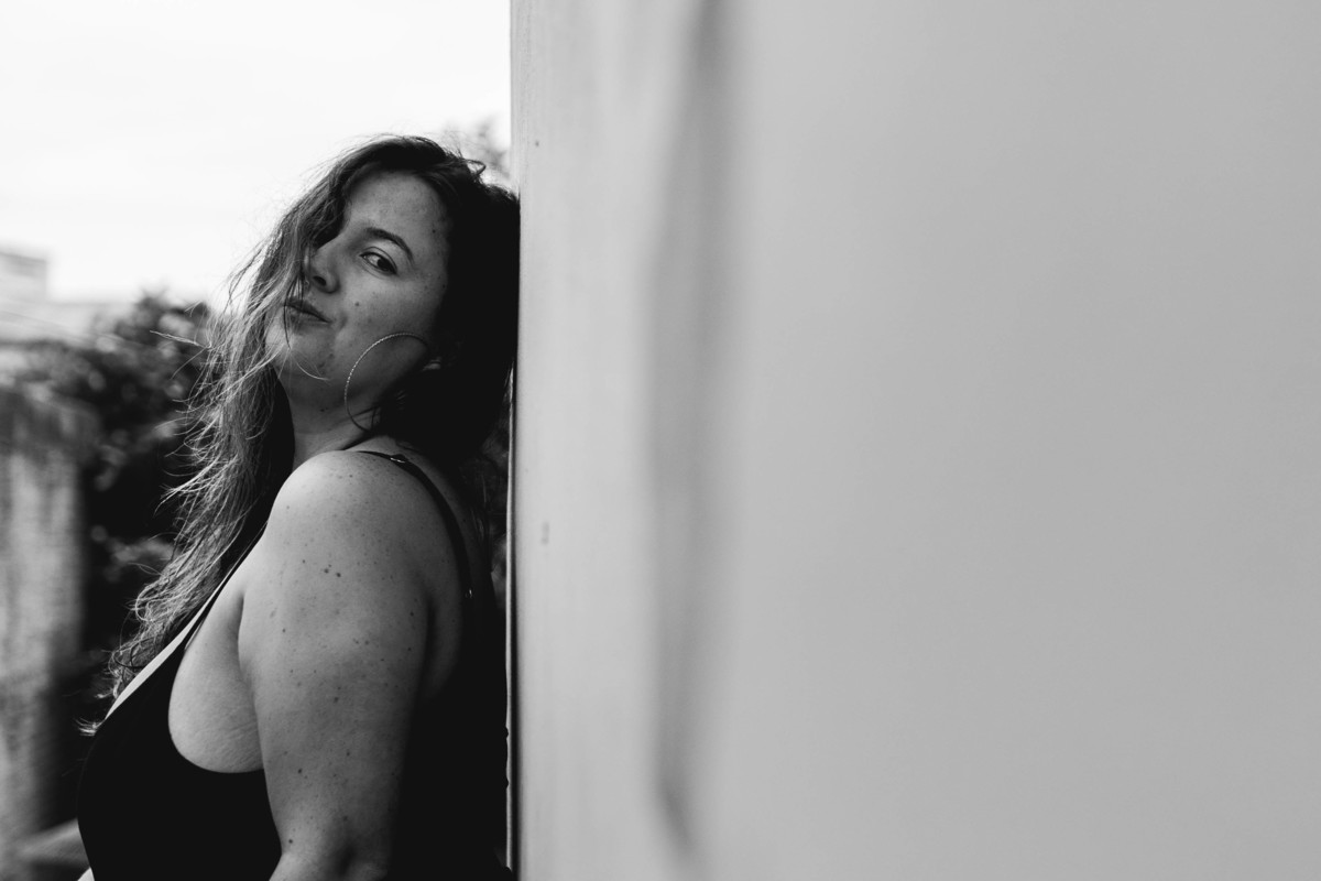 foto em preto e branco de mulher encostada na parede com o cabelo tampando metade do rosto e olhando para a câmera