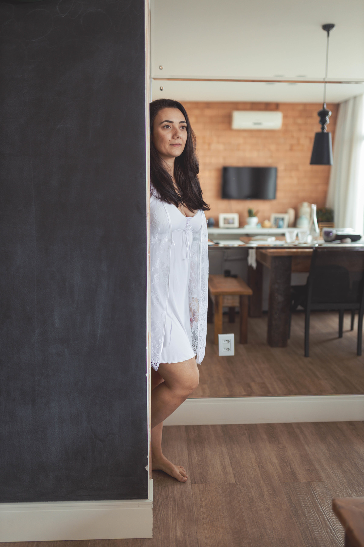 foto de mulher de camisola e hobby  branco encostada na parede olhando pra frente e sorrindo