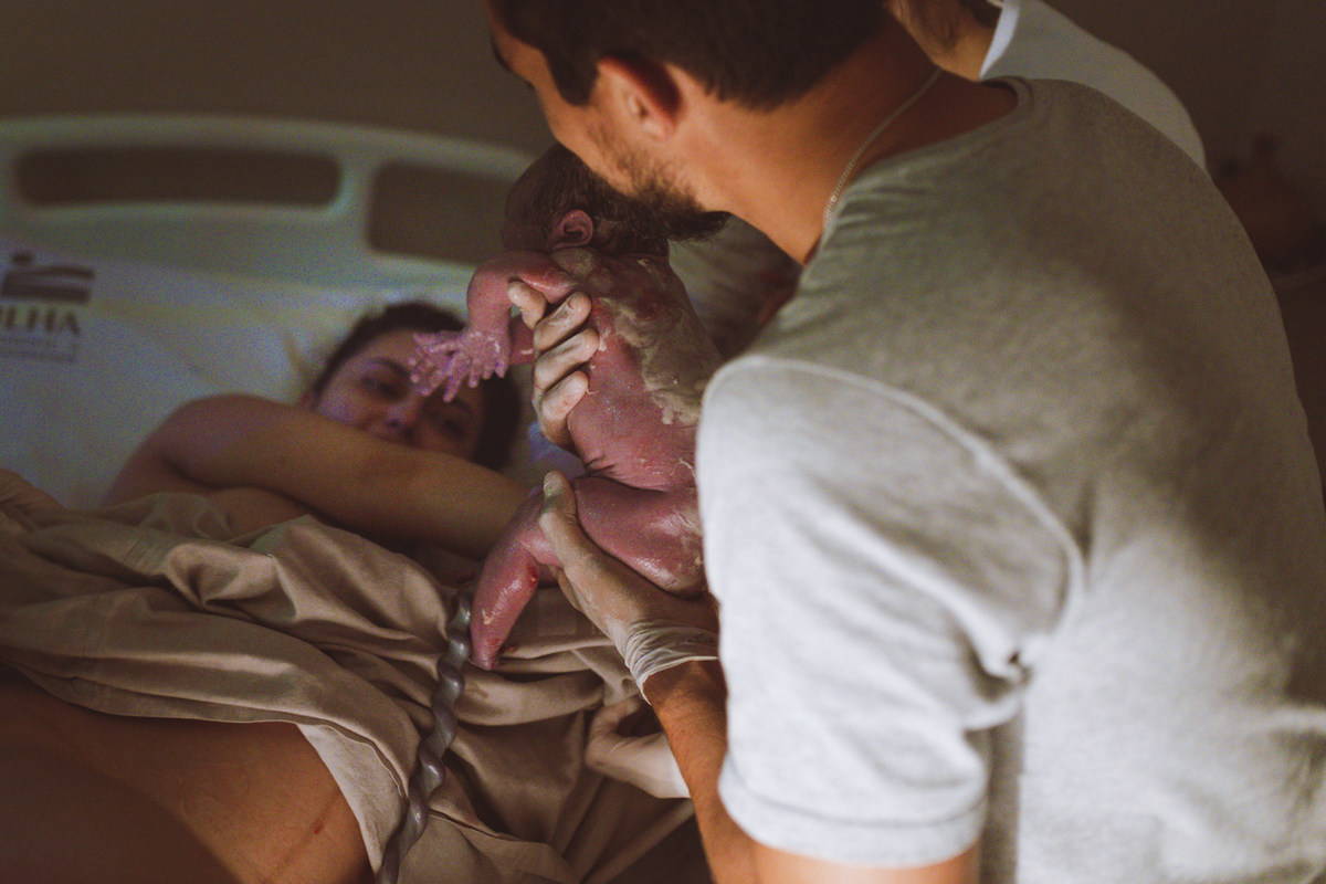 pai entregando o bebê à mãe logo após ter recebido a criança no nascimento em maternidade em Florianópolis