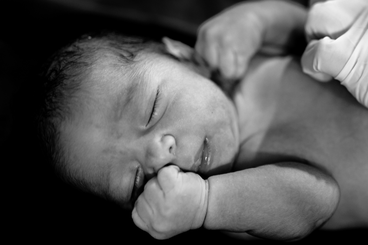 bebê com as mãozinhas fechadas deitado no berço aquecido após nascer na maternidade em Florianópolis. foto em preto e branco
