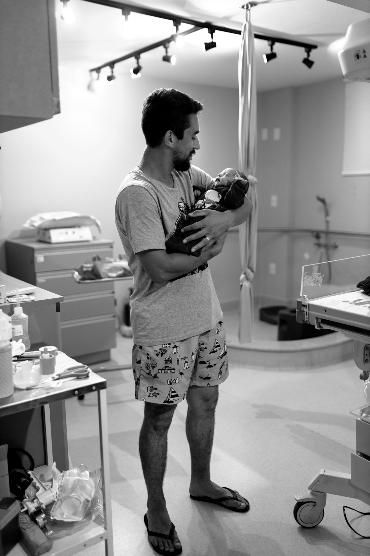 pai carregando bebê no colo pela primeira vez após nascer. Foto em preto e braco na sala de parto da maternidade de Florianópolis