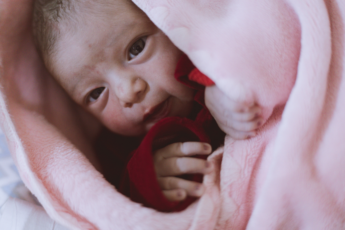 bebê recém nascida de roupa vermelha enrolada em manta rosa na maternidade em Florianópolis. 